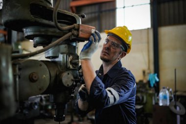 Torna operatörü işine odaklandı. Üniformalı ve kasklı işçiler torna tezgahında çalışıyor, fabrikada. Endüstriyel üretim, metal mühendisliği, imalat.
