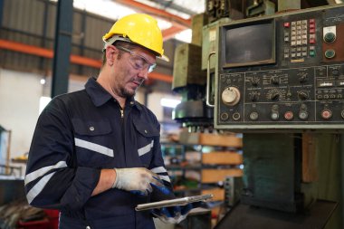 Torna operatörü işine odaklandı. Üniformalı ve kasklı işçiler torna tezgahında çalışıyor, fabrikada. Endüstriyel üretim, metal mühendisliği, imalat.