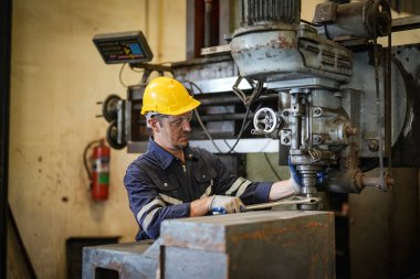 Torna operatörü işine odaklandı. Üniformalı ve kasklı işçiler torna tezgahında çalışıyor, fabrikada. Endüstriyel üretim, metal mühendisliği, imalat.