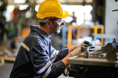 Torna operatörü işine odaklandı. Üniformalı ve kasklı işçiler torna tezgahında çalışıyor, fabrikada. Endüstriyel üretim, metal mühendisliği, imalat.