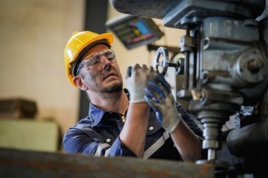 Torna operatörü işine odaklandı. Üniformalı ve kasklı işçiler torna tezgahında çalışıyor, fabrikada. Endüstriyel üretim, metal mühendisliği, imalat.