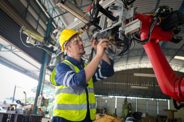 Erkek teknisyen bir robot kolu dijital tabletle programlar ve bir fabrikada robot montajı yapar. Fabrikada çıraklık mühendisliği programlayan robotlar..