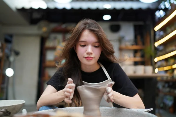漂亮的围裙女工匠坐在陶瓷轮旁 用手工工具塑造湿黏土器皿的特写 — 图库照片