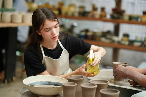 聚精会神漂亮的围裙女工匠坐在陶瓷轮旁 用手工工具塑造湿黏土器皿的特写 — 图库照片