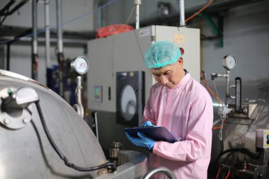 Yiyecek ve içecek endüstrisinde çalışan Asyalı bir işçi. İçecek İşlem Kontrol Üretim Hattı Taşıyıcısı Denetleniyor