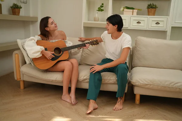 stock image young woman playing guitar to her husband at home 