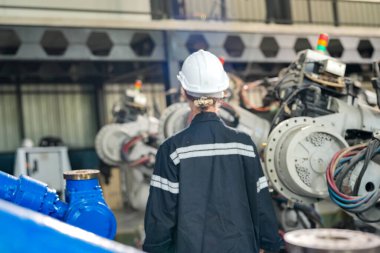 Teknisyen bir robot kolu dijital tabletle programlar ve bir fabrikada robot montajı yapar. Çırak mühendisleri fabrikada robot programlıyorlar..