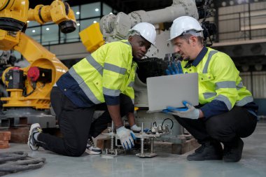 technicians programming  a robot arm in a factory. Apprentice engineers programming robot in factory. clipart