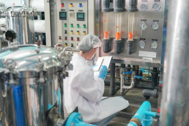 Elektrik santrali için ters osmoz sisteminde çalışan bir kadın. Endüstri için RO sistemi, endüstriyel kimyasallar, enerji santrali, petrol ve gaz gibi borularla kurulması popüler ekipmanlar. Şişeleme fabrikasında su şişelerini kontrol eden genç ve mutlu bir kadın işçi. 