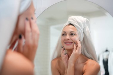 Cilt bakım konsepti. Aynaya bakan, dokunan bir kadın ve tuvalette mükemmel bir ten. Seçici Odaklanma