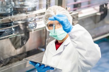 Elektrik santrali için ters osmoz sisteminde çalışan bir kadın. Endüstri için RO sistemi, endüstriyel kimyasallar, enerji santrali, petrol ve gaz gibi borularla kurulması popüler ekipmanlar. Şişeleme fabrikasında genç bayan işçi su şişelerini kontrol ediyor.