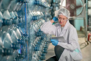 Elektrik santrali için ters osmoz sisteminde çalışan bir kadın. Endüstri için RO sistemi, endüstriyel kimyasallar, enerji santrali, petrol ve gaz gibi borularla kurulması popüler ekipmanlar. Şişeleme fabrikasında su şişelerini kontrol eden genç ve mutlu bir kadın işçi. 