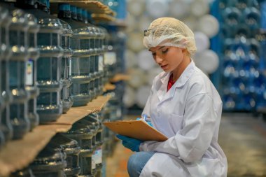 Elektrik santrali için ters osmoz sisteminde çalışan bir kadın. Endüstri için RO sistemi, endüstriyel kimyasallar, enerji santrali, petrol ve gaz gibi borularla kurulması popüler ekipmanlar. Şişeleme fabrikasında genç bayan işçi su şişelerini kontrol ediyor.