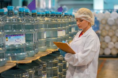 Elektrik santrali için ters osmoz sisteminde çalışan bir kadın. Endüstri için RO sistemi, endüstriyel kimyasallar, enerji santrali, petrol ve gaz gibi borularla kurulması popüler ekipmanlar. Şişeleme fabrikasında genç bayan işçi su şişelerini kontrol ediyor. 