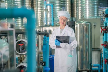 Elektrik santrali için ters osmoz sisteminde çalışan bir kadın. Endüstri için RO sistemi, endüstriyel kimyasallar, enerji santrali, petrol ve gaz gibi borularla kurulması popüler ekipmanlar. Şişeleme fabrikasında su şişelerini kontrol eden genç ve mutlu bir kadın işçi. 