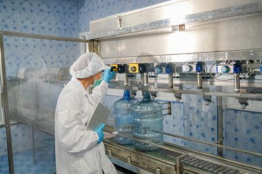 Elektrik santrali için ters osmoz sisteminde çalışan bir kadın. Endüstri için RO sistemi, endüstriyel kimyasallar, enerji santrali, petrol ve gaz gibi borularla kurulması popüler ekipmanlar. Şişeleme fabrikasında su şişelerini kontrol eden genç ve mutlu bir kadın işçi. 