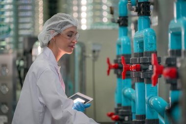 Elektrik santrali için ters osmoz sisteminde çalışan bir kadın. Endüstri için RO sistemi, endüstriyel kimyasallar, enerji santrali, petrol ve gaz gibi borularla kurulması popüler ekipmanlar. Şişeleme fabrikasında su şişelerini kontrol eden genç ve mutlu bir kadın işçi. 