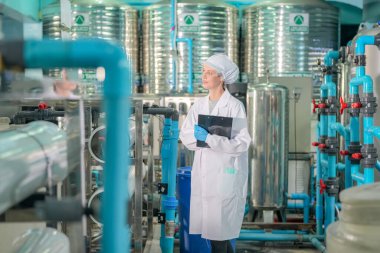 Elektrik santrali için ters osmoz sisteminde çalışan bir kadın. Endüstri için RO sistemi, endüstriyel kimyasallar, enerji santrali, petrol ve gaz gibi borularla kurulması popüler ekipmanlar. Şişeleme fabrikasında su şişelerini kontrol eden genç ve mutlu bir kadın işçi. 