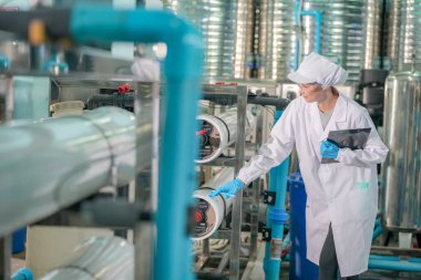 Elektrik santrali için ters osmoz sisteminde çalışan bir kadın. Endüstri için RO sistemi, endüstriyel kimyasallar, enerji santrali, petrol ve gaz gibi borularla kurulması popüler ekipmanlar. Şişeleme fabrikasında su şişelerini kontrol eden genç ve mutlu bir kadın işçi. 