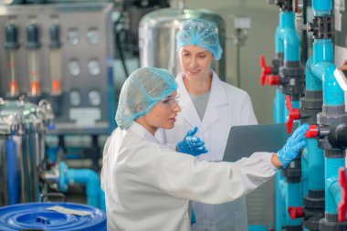 Elektrik santrali için ters osmoz sisteminde çalışan kadınlar. Endüstri için RO sistemi, endüstriyel kimyasallar, enerji santrali, petrol ve gaz gibi borularla kurulması popüler ekipmanlar. Şişeleme fabrikasında genç bayan işçiler su şişelerini kontrol ediyor. 