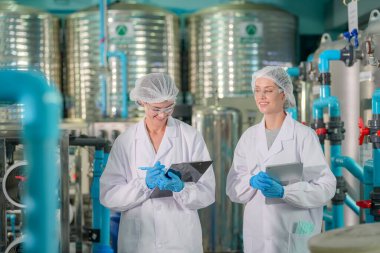 Elektrik santrali için ters osmoz sisteminde çalışan bir kadın. Endüstriyel endüstri için RO sistemi, endüstriyel kimyasallar, elektrik santrali gibi borularla kurulması popüler ekipmanlar. Şişeleme fabrikasında su şişelerini kontrol eden genç ve mutlu bir kadın işçi.  