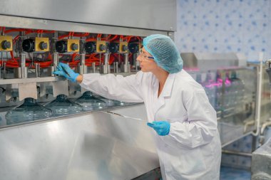 Elektrik santrali için ters osmoz sisteminde çalışan bir kadın. Endüstri için RO sistemi, endüstriyel kimyasallar, enerji santrali, petrol ve gaz gibi borularla kurulması popüler ekipmanlar. Şişeleme fabrikasında genç bayan işçi su şişelerini kontrol ediyor.  