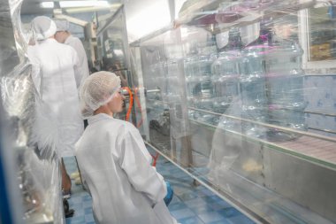 Elektrik santrali için ters osmoz sisteminde çalışan bir kadın. Endüstri için RO sistemi, endüstriyel kimyasallar, enerji santrali, petrol ve gaz gibi borularla kurulması popüler ekipmanlar. Şişeleme fabrikasında genç bayan işçi su şişelerini kontrol ediyor.
