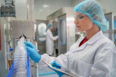 Elektrik santrali için ters osmoz sisteminde çalışan bir kadın. Endüstri için RO sistemi, endüstriyel kimyasallar, enerji santrali, petrol ve gaz gibi borularla kurulması popüler ekipmanlar. Şişeleme fabrikasında genç bayan işçi su şişelerini kontrol ediyor.