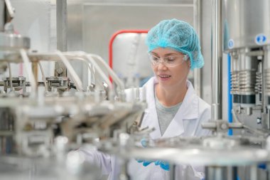 Elektrik santrali için ters osmoz sisteminde çalışan bir kadın. Endüstri için RO sistemi, endüstriyel kimyasallar, enerji santrali, petrol ve gaz gibi borularla kurulması popüler ekipmanlar. Şişeleme fabrikasında su şişelerini kontrol eden genç ve mutlu bir kadın işçi. 