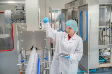 Elektrik santrali için ters osmoz sisteminde çalışan bir kadın. Endüstri için RO sistemi, endüstriyel kimyasallar, enerji santrali, petrol ve gaz gibi borularla kurulması popüler ekipmanlar. Şişeleme fabrikasında genç bayan işçi su şişelerini kontrol ediyor. 