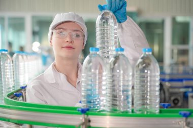 Elektrik santrali için ters osmoz sisteminde çalışan bir kadın. Endüstri için RO sistemi, endüstriyel kimyasallar, enerji santrali, petrol ve gaz gibi borularla kurulması popüler ekipmanlar. Şişeleme fabrikasında su şişelerini kontrol eden genç ve mutlu bir kadın işçi.