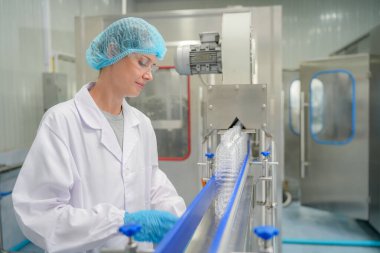 Elektrik santrali için ters osmoz sisteminde çalışan bir kadın. Endüstri için RO sistemi, endüstriyel kimyasallar, enerji santrali, petrol ve gaz gibi borularla kurulması popüler ekipmanlar. Şişeleme fabrikasında su şişelerini kontrol eden genç ve mutlu bir kadın işçi. 