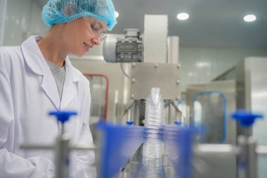 Elektrik santrali için ters osmoz sisteminde çalışan bir kadın. Endüstri için RO sistemi, endüstriyel kimyasallar, enerji santrali, petrol ve gaz gibi borularla kurulması popüler ekipmanlar. Şişeleme fabrikasında genç bayan işçi su şişelerini kontrol ediyor.
