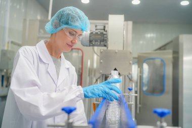 Elektrik santrali için ters osmoz sisteminde çalışan bir kadın. Endüstri için RO sistemi, endüstriyel kimyasallar, enerji santrali, petrol ve gaz gibi borularla kurulması popüler ekipmanlar. Şişeleme fabrikasında genç bayan işçi su şişelerini kontrol ediyor.