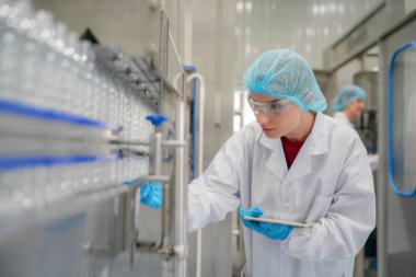 Elektrik santrali için ters osmoz sisteminde çalışan bir kadın. Endüstri için RO sistemi, endüstriyel kimyasallar, enerji santrali, petrol ve gaz gibi borularla kurulması popüler ekipmanlar. Şişeleme fabrikasında genç bayan işçi su şişelerini kontrol ediyor. 