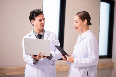 İki genç doktorun dizüstü bilgisayar kullanırken ve modern bir ofiste tartışırken görüntüsü.