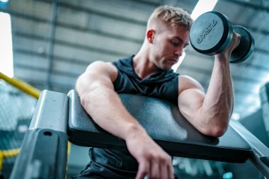 Erkek sporcu spor salonunda egzersiz yapıyor, ağırlık kaldırıyor, eklemlerini çekiyor..