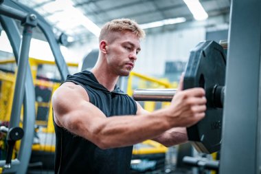 Erkek sporcu spor salonunda egzersiz yapıyor, ağırlık kaldırıyor, eklemlerini çekiyor..