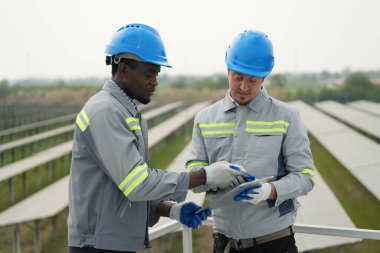 Fotovoltaik bir çiftlikte çalışan elektrik mühendisleri, güneş enerjisi endüstrisindeki aletlerle kontrol ve bakım ekipmanlarını kontrol ediyorlar..