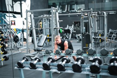 Erkek sporcu spor salonunda egzersiz yapıyor, ağırlık kaldırıyor, eklemlerini çekiyor..