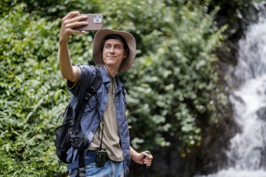 Genç adam fotoğraf çekiyor, ormanda yürüyüş yaparken eğleniyor.