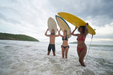 Genç kadınlar ve erkek sörfçüler sahilde eğleniyorlar.