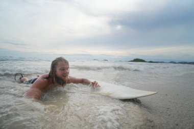 Genç adam sörf tahtasında yüzüyor.