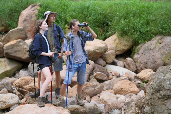 Hikers walking along a trail on a mountain with hiking sticks. Adventure, travel, tourism, hike and people concept. Group of smiling friends with backpacks outdoors.