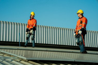 Uzman teknisyen profesyonel mühendis güneş ışığı altında fabrikanın çatısına güneş paneli kurarken üst görüntüyü kontrol ediyor. Elektrik yenilenebilir eko enerji hizmeti veren mühendisler