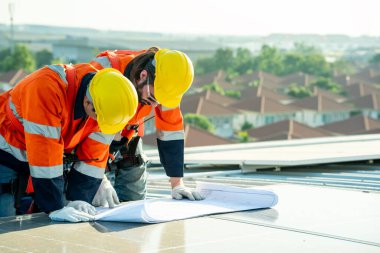 Uzman teknisyen profesyonel mühendis güneş ışığı altında fabrikanın çatısına güneş paneli kurarken üst görüntüyü kontrol ediyor. Elektrik yenilenebilir eko enerji hizmeti veren mühendisler
