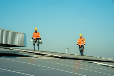 Uzman teknisyen profesyonel mühendis güneş ışığı altında fabrikanın çatısına güneş paneli kurarken üst görüntüyü kontrol ediyor. Elektrik yenilenebilir eko enerji hizmeti veren mühendisler