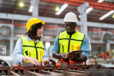 Modern fabrikanın üretim bölümünde iş tulumu ve şapka giyen ve fikirleri tartışan iki profesyonel teknisyen.  