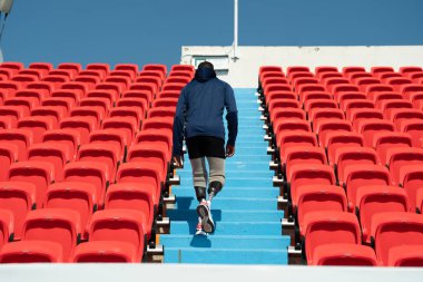 Stadyumdaki koşu pistinde protez bıçaklı Asyalı atletler. Futbol stadyumundaki koltuklar