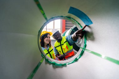 Modern fabrikanın üretim bölümünde iş tulumu ve şapka giyen ve fikirleri tartışan iki profesyonel teknisyen.  